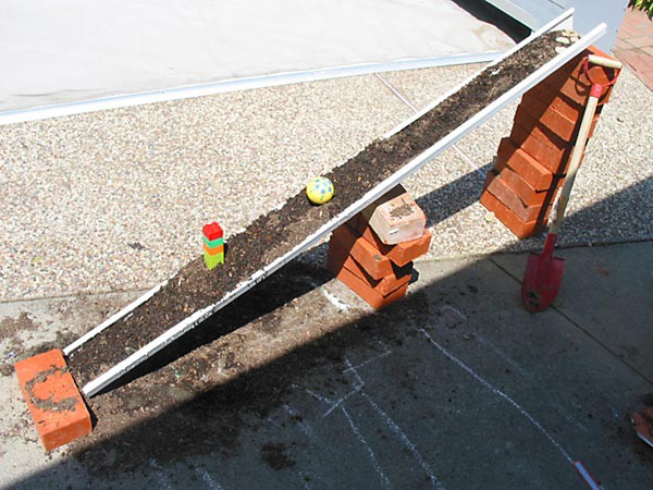 A rubber ball and model tower are placed on a slope made from soil that has been packed into a gutter