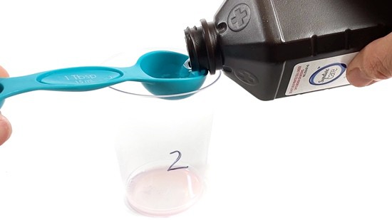 A person fills a tablespoon with  hydrogen peroxide. 