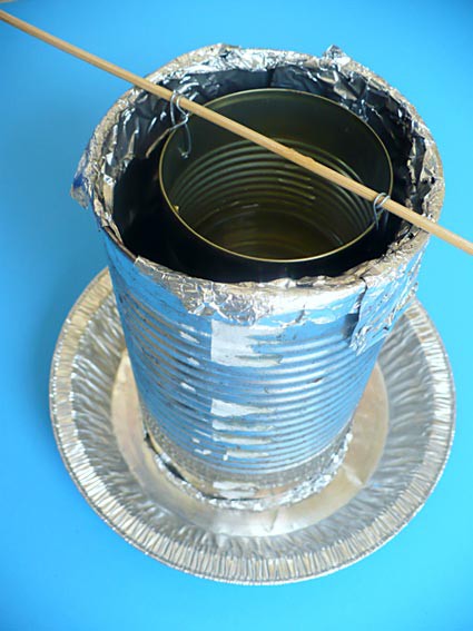 A small can is suspended within the opening of a larger can with metal wires and a wooden dowel