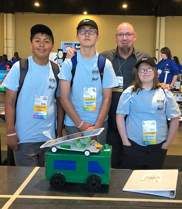 Three students and a teacher stand in front of a solar-powered car