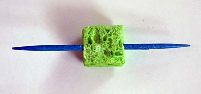 A blue toothpick is inserted through a small square piece of sponge