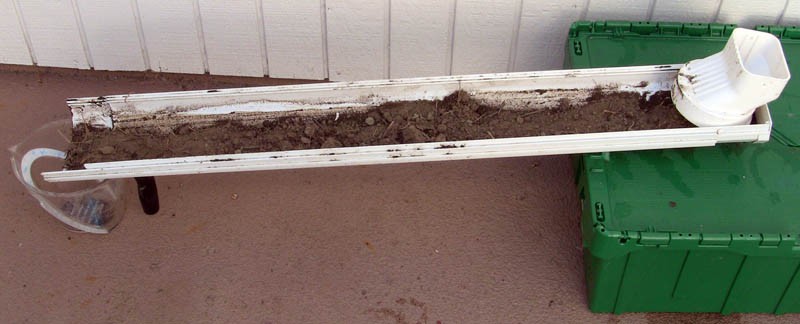 A rain gutter is filled with soil and placed on a slope with a measuring cup under the lowest end