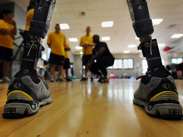 The view of several men in the distance in a gym as seen when looking between two metal prosthetic legs encased in sneakers.