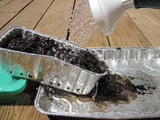 Water is poured over an aluminum bread pan filled with soil that has been placed on an incline