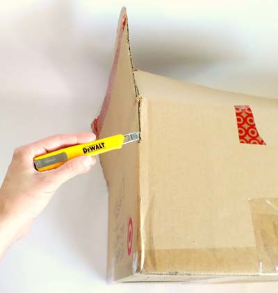 The edge of a cardboard box where two walls meet is cut with a utility knife