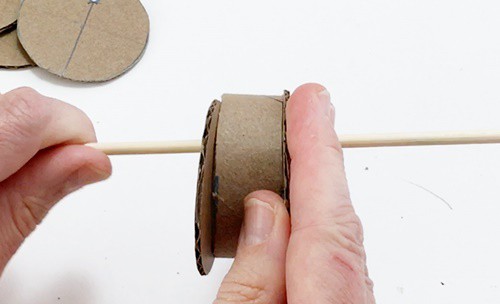  A short section of cardboard tube being pressed against a circle. The circle and the tube are both threaded on a skewer.  