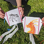 Two students holding the paper kites they made, decorated, and tested as part of a science activity