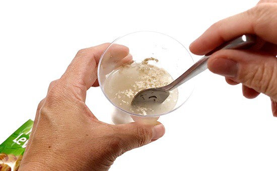 A person stirs a solution of instant yeast in water with a spoon.