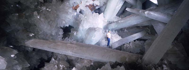 A man stands on giant crystalized spikes formed in a cave