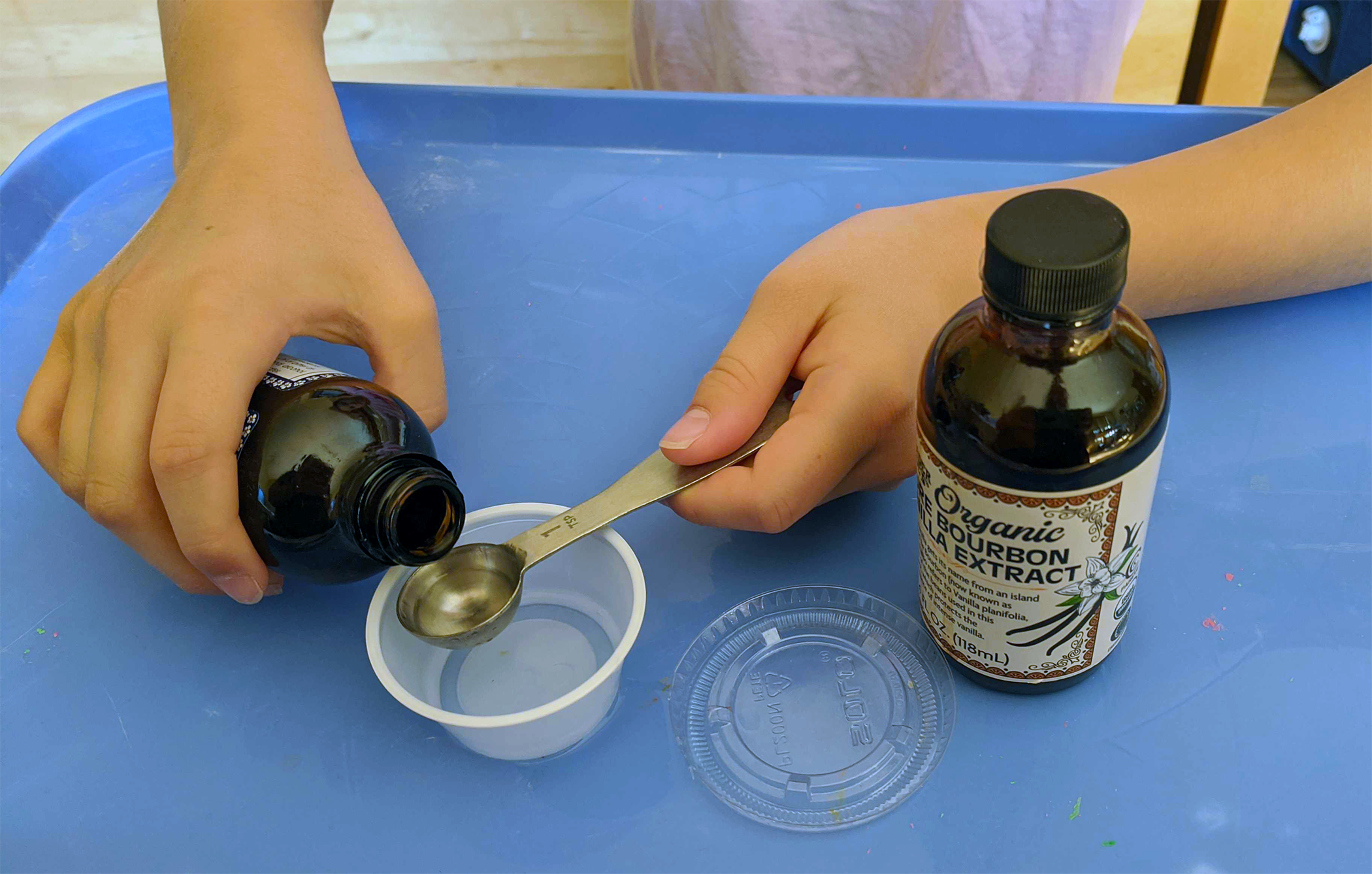 Student measuring vanilla and pouring it into a small plastic cup for an odor memory smell test