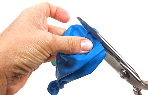 A person is cutting off the tip of a deflated balloon using scissors.