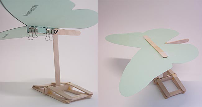 Binder clips hold a paper butterfly cutout on a popsicle stick support structure