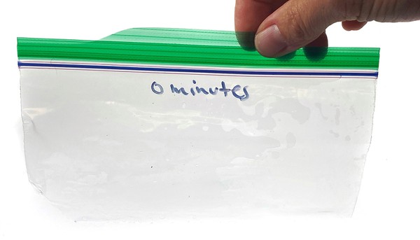 A hand holds a resealable plastic bag that has the left bottom corner cut off. 