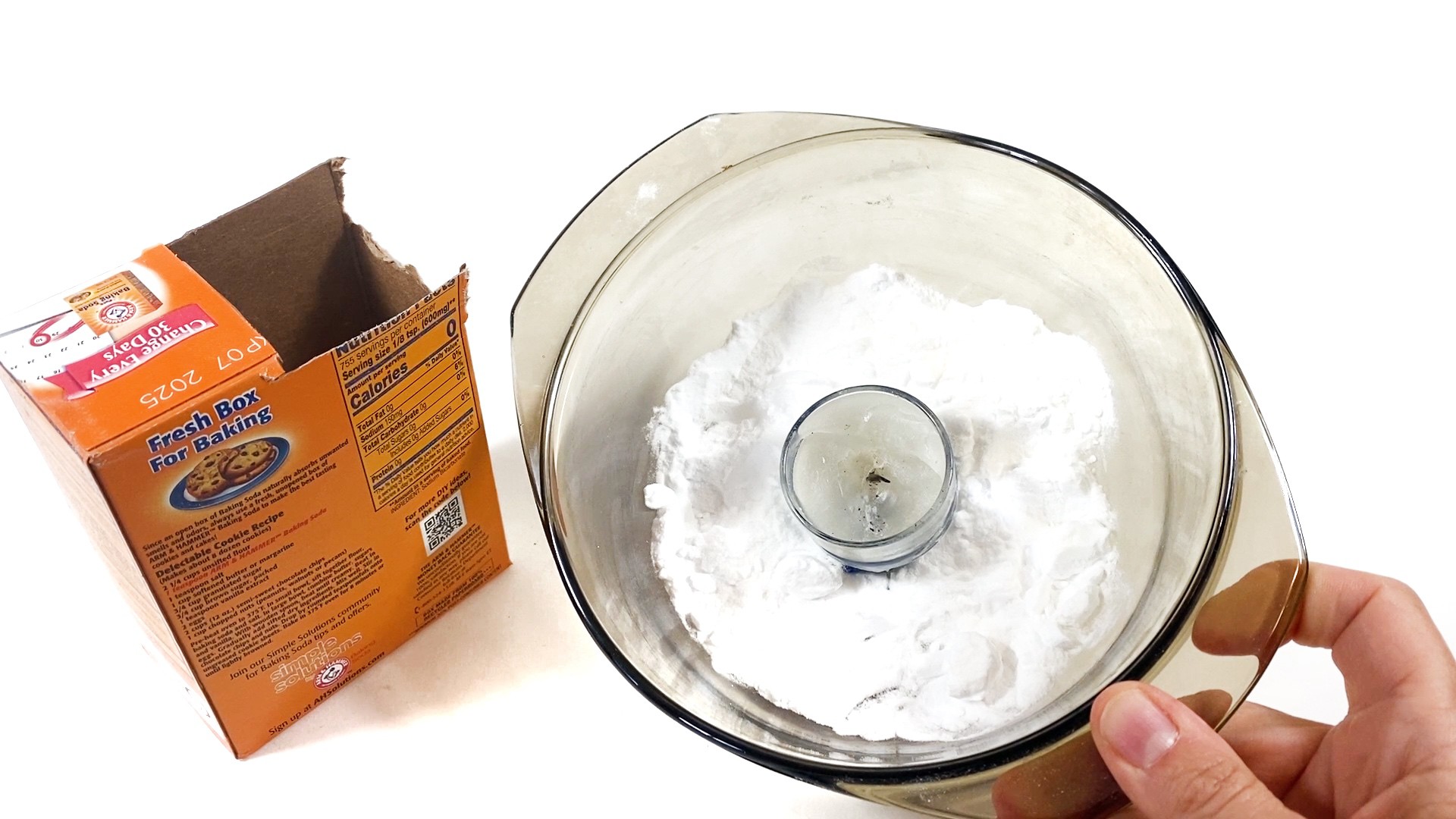 The image shows a bowl with a candle inside next to a container of baking soda. Baking soda is sprinkled around the candle in the bowl.