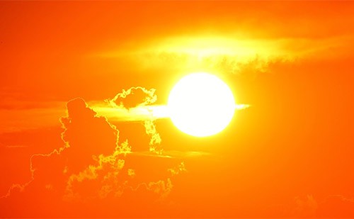 Photo of the sun shining bright orange between the clouds