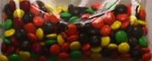 Clear bag full of green, yellow, brown, orange, and red M&Ms in near equal proportions. 