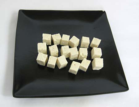 Tofu is cut into eighteen uniform cubes and placed on a plate
