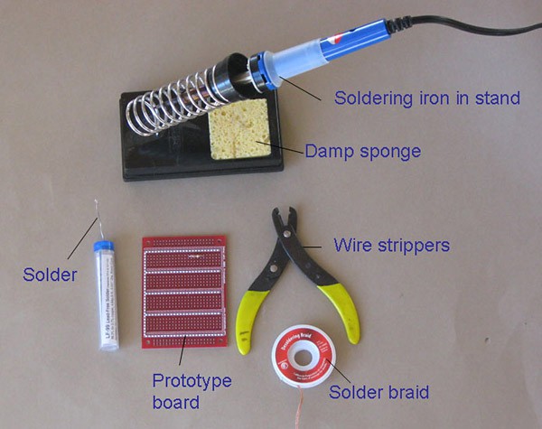 A soldering iron with stand, damp sponge, solder, prototype board, solder braid and wire strippers