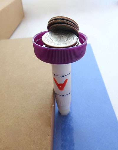A bottlecap filled with coins rests on the top of a tube of lip balm