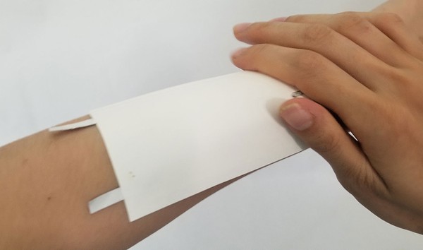Firmly pressing on temporary tattoo onto forearm. 