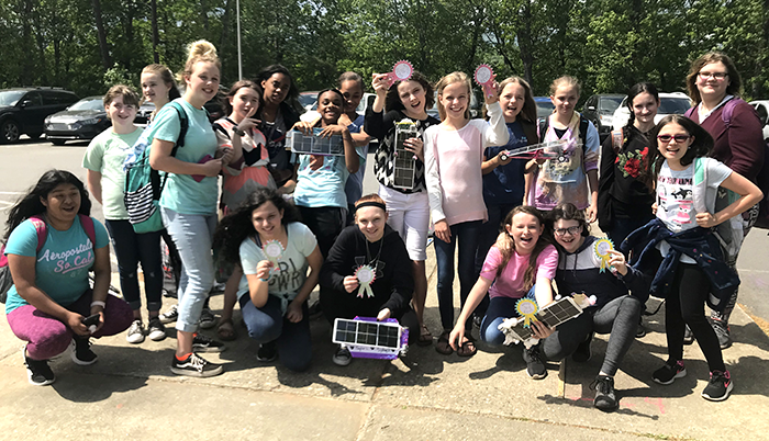 Students from an all-girl STEM club holding solar-powered cars