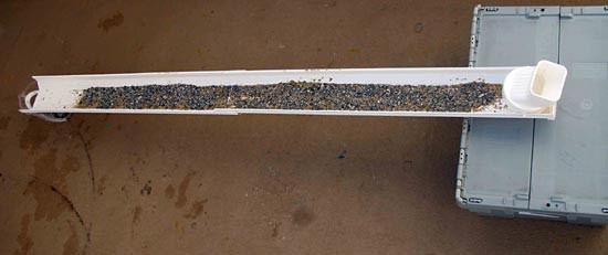Small gravel is spread evenly over a layer of sand in a rain gutter