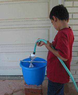 A child uses a hose to pour water onto a waterwheel in a bucket