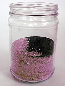 Pink sand and iron filings are placed in a glass jar