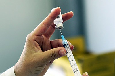 Drawing fluid into a needle from a vaccine vial in order to vaccinate a patient.   