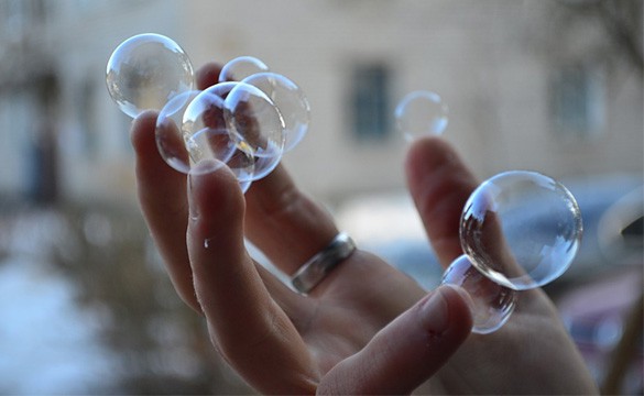 Large bubbles rest on a persons fingertips without popping