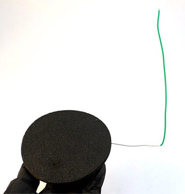 A green wire is stripped and inserted into a thin circular anode pad