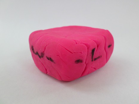 A cube of pink Play-Doh, with a 'W' and 'L' on the sides, squished down