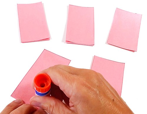 Three paper strips on a table. Hands holding a gluestick and applying glue to an additional paper strip.  