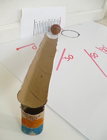 A cardboard tube is cut length wise and raised on one end to form a ramp that a model basketball will roll down