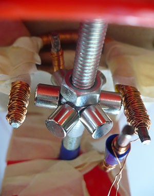 Six magnets on a hex nut sit inline with and between two prongs of an iron core that has been bent into a U shape