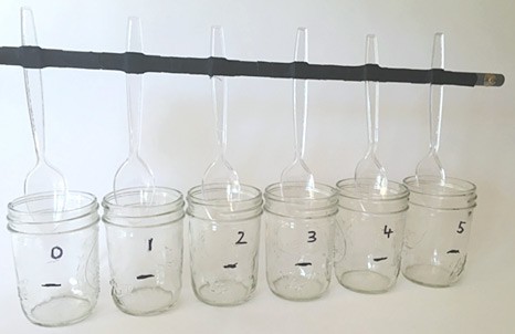 Six plastic spoons are attached to a stick and inserted simultaneously into six mason jars