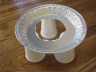 Three upside down cups support an aluminum pie pan with a hole cut through the center