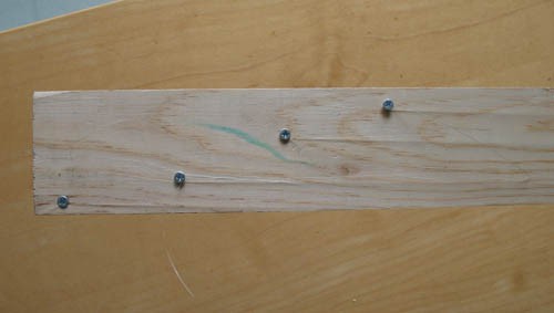 Four screws are placed diagonally on the length of a wooden plank starting from the bottom left and ending in the top right