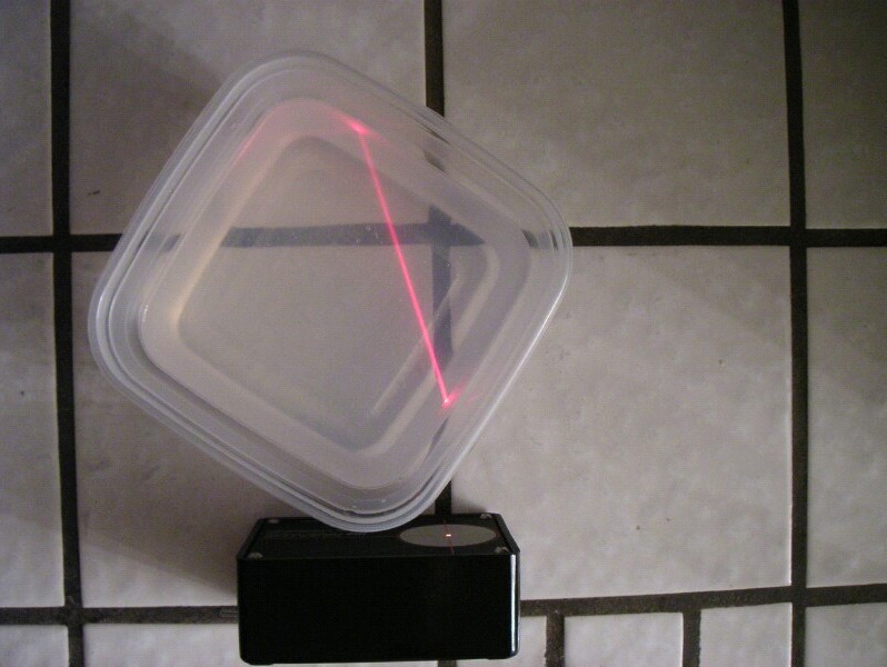 A red beam of light is visible as it passes through a plastic container filled with a clear liquid