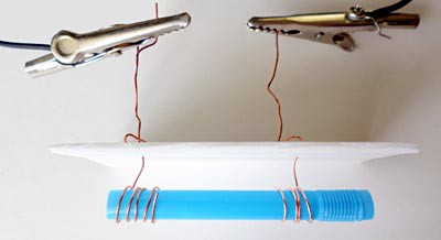 Two alligator clips connect to two copper wires pushed through a styrofoam sheet and wrapped around the ends of a cut straw
