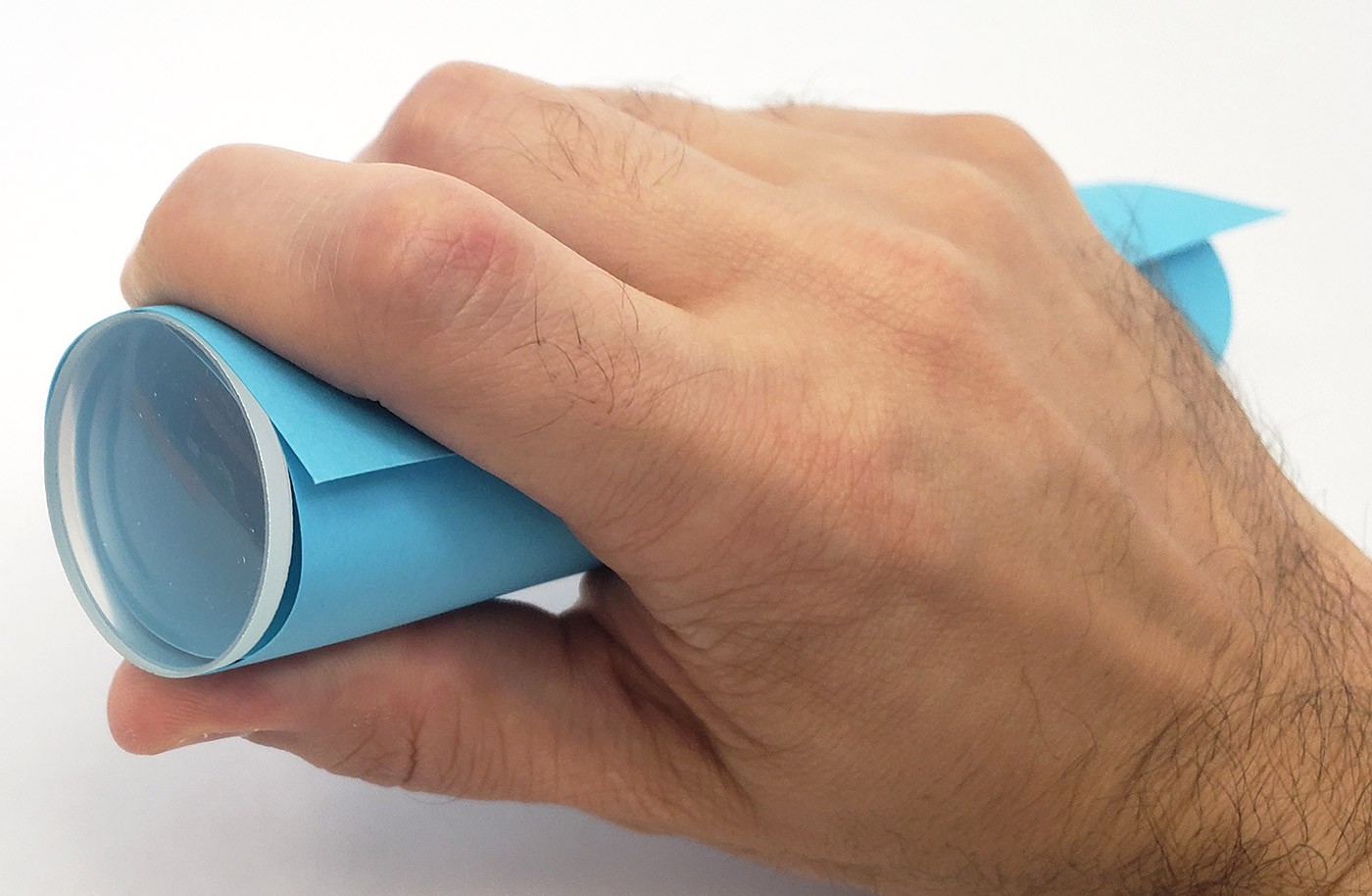 A hand holding a piece of cardstock rolled into a tube so it is the same diameter as the lens