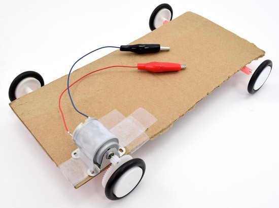 A motor is aligned with the gears on the axle of a solar powered car and secured with tape