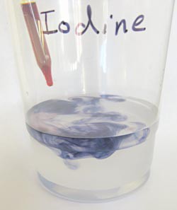 Liquid from an eye dropper reacts with clear liquid in a plastic cup turning the clear liquid blue