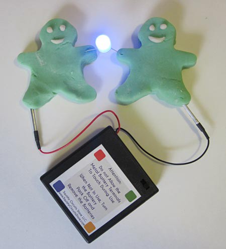 A lit LED connects the hands of two play dough figures that each have a lead of a battery pack inserted into their leg