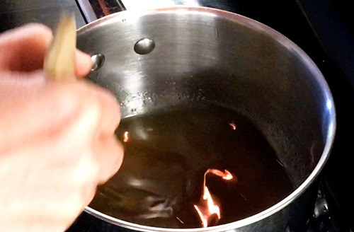 Person stirring in a saucepan containing  translucent sugar syrup. 