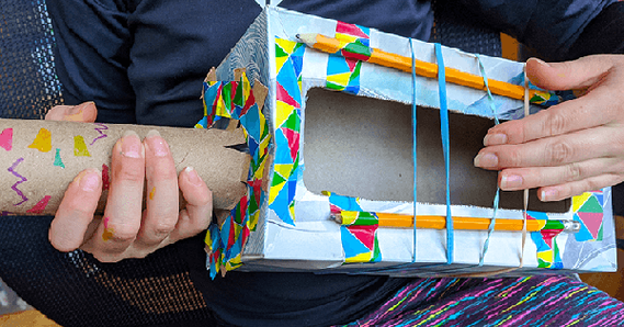 Student holding rubber band guitar made from cardboard box
