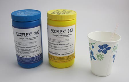 A blue and yellow container of two part silicon rubber next to a paper cup