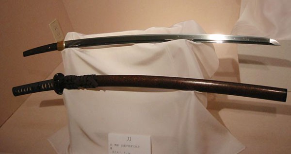 A sheathed and unsheathed katana rest on a stand covered by a white cloth