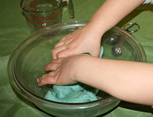 Two hands knead green clay in a bowl