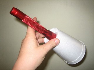 The head of a flashlight is inserted through a hole cut at the bottom of a styrofoam cup